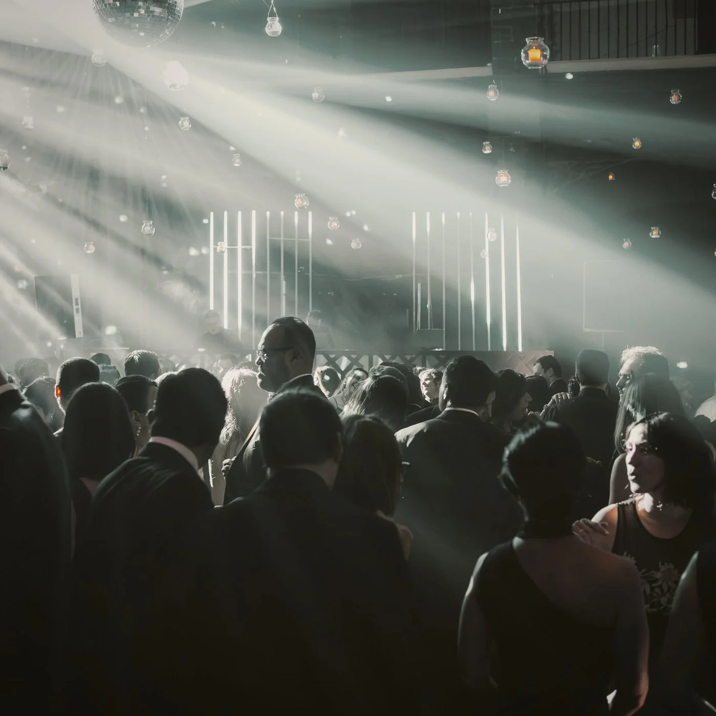 Pista llena durante la fiesta de una boda, con haces de luz y cabina de DJ al fondo