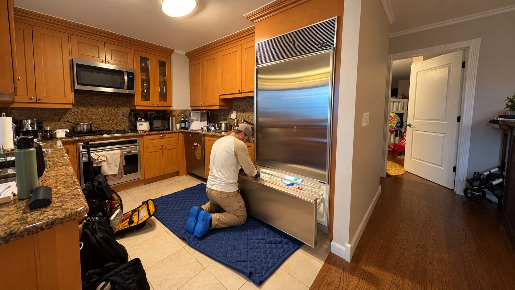 Sub-Zero technician in disposable blue shoe covers working on a freezer over a protective floor blanket in a Manhattan home