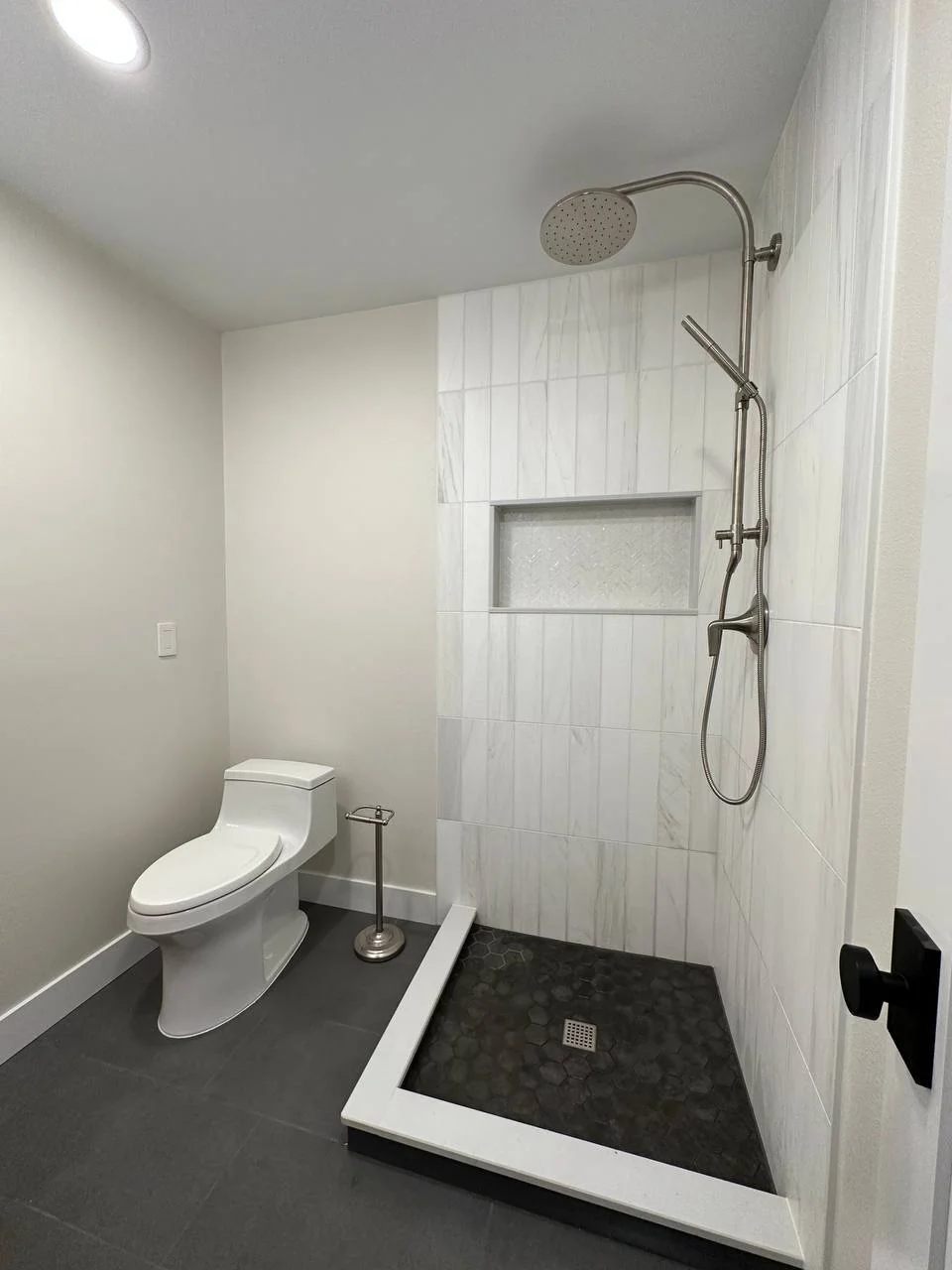 White tile shower with black hex tile floor