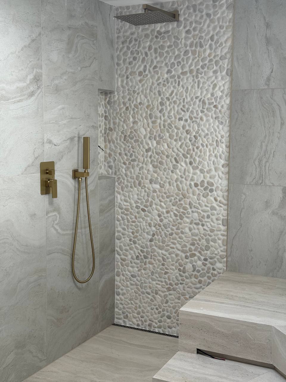 Custom shower with pebble accent wall and brass fixtures