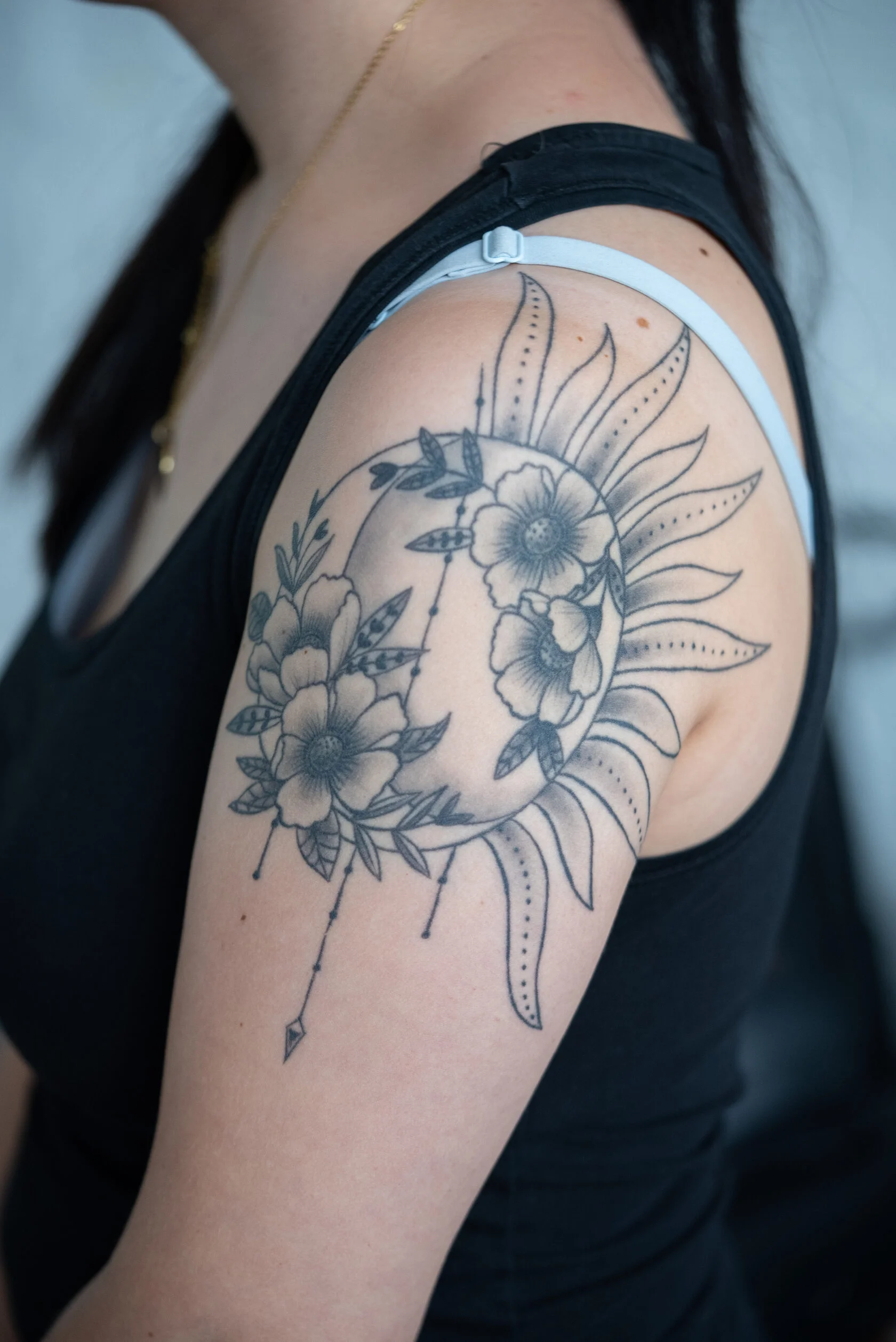 Feinliniges Sonne-Mond-Blumen-Tattoo am Oberarm, frisch gestochen