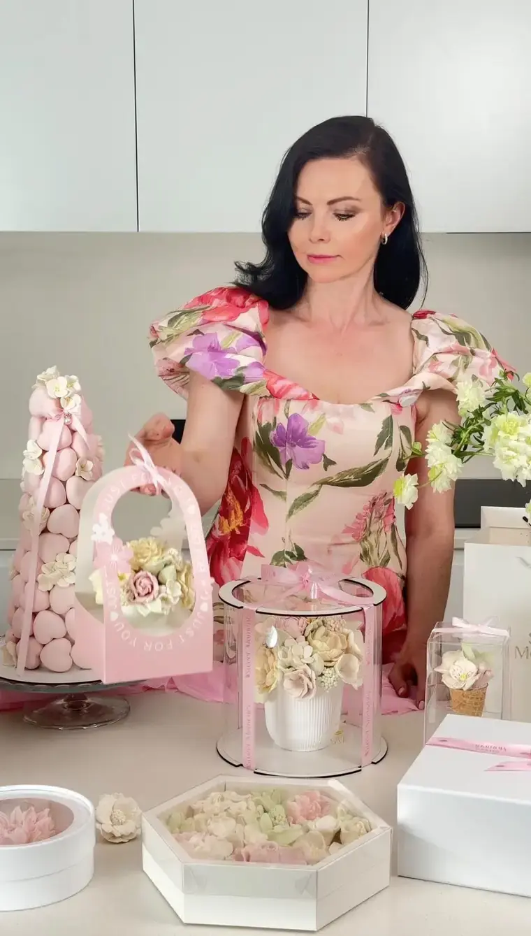 Natalia holding a handmade pink gift basket of zefir flowers, surrounded by finished boxed arrangements
